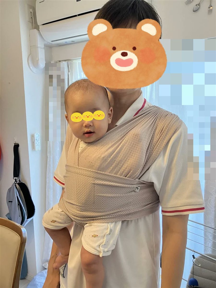 家の中で、コニーの抱っこ紐で息子を抱っこするパパ。XS が小さく、息子が横にずれている